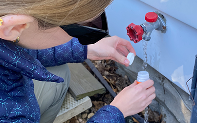 A person collecting a Water Sample from a spigot on the side of a house